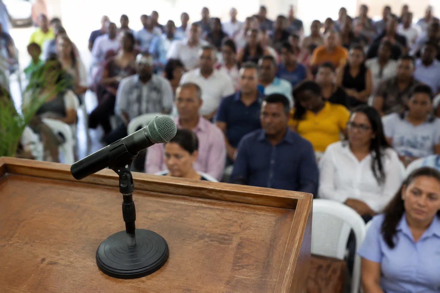Microfone sobre uma tribuna, com a plateia sentada desfocada ao fundo
